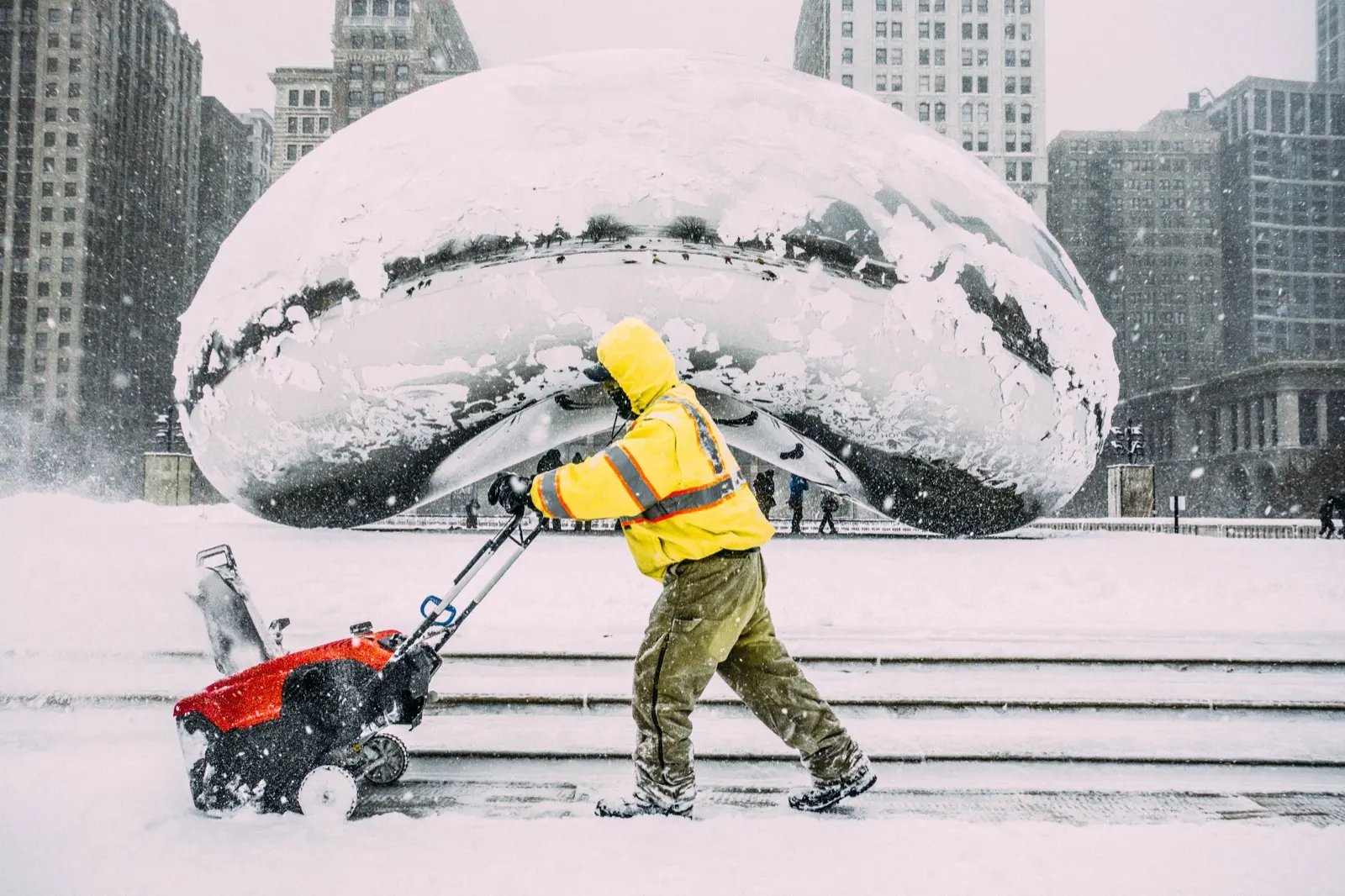 Cloud Gate, First Snow — a lone worker in yellow clearing snow beneath the Bean